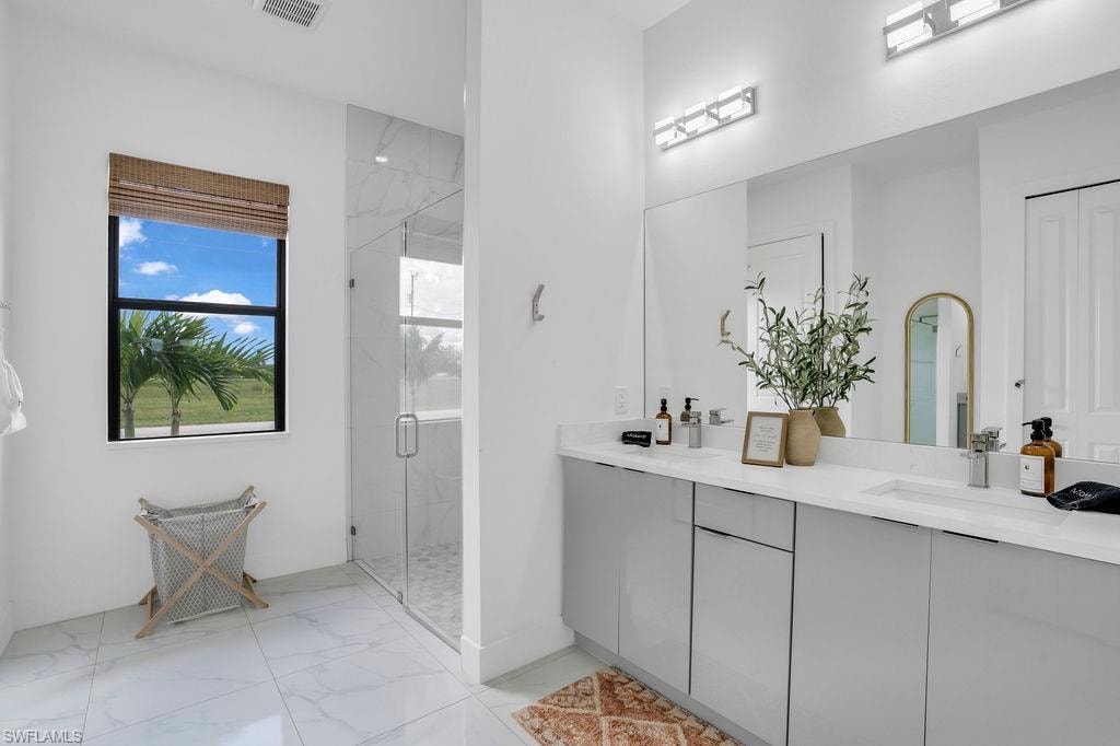 Full bathroom featuring light marble finish flooring, a marble finish shower, and double vanity