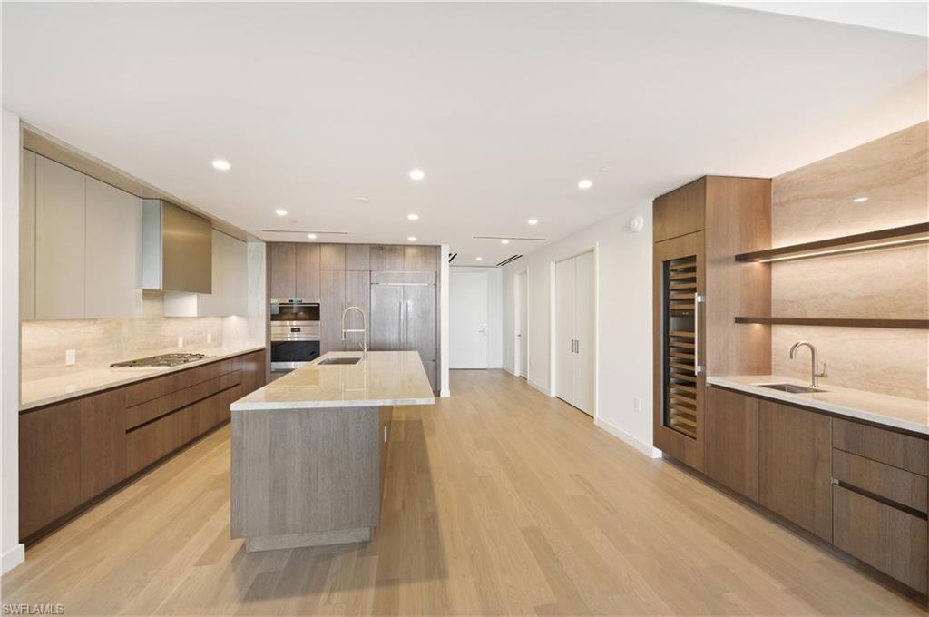Gas cooktop, wine fridge, wet bar with lighted shelves & bar stool counter seating.