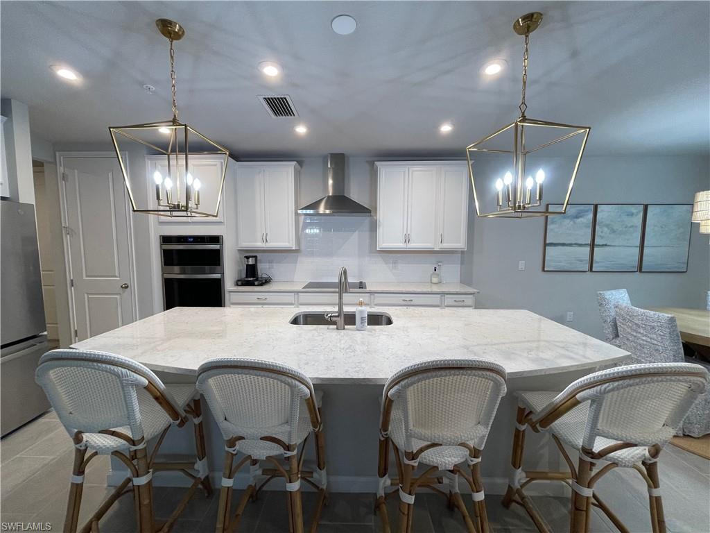 Kitchen with a chandelier, a breakfast bar, stainless steel appliances, white cabinets, and wall chimney exhaust hood