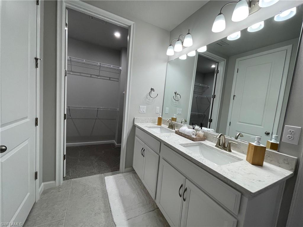 Bathroom featuring a walk in closet, double vanity, and light tile patterned floors