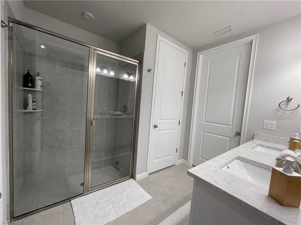 Bathroom with double vanity, light tile patterned floors, and a stall shower