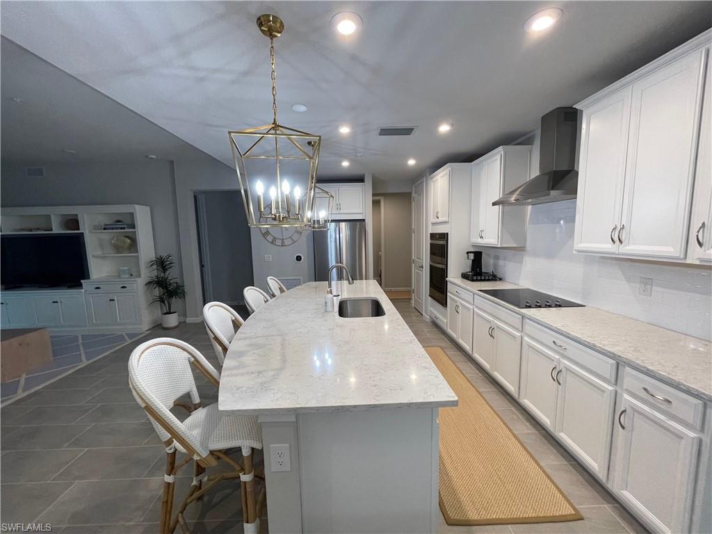Kitchen featuring a breakfast bar area, a center island with sink, white cabinets, light stone counters, and hanging light fixtures