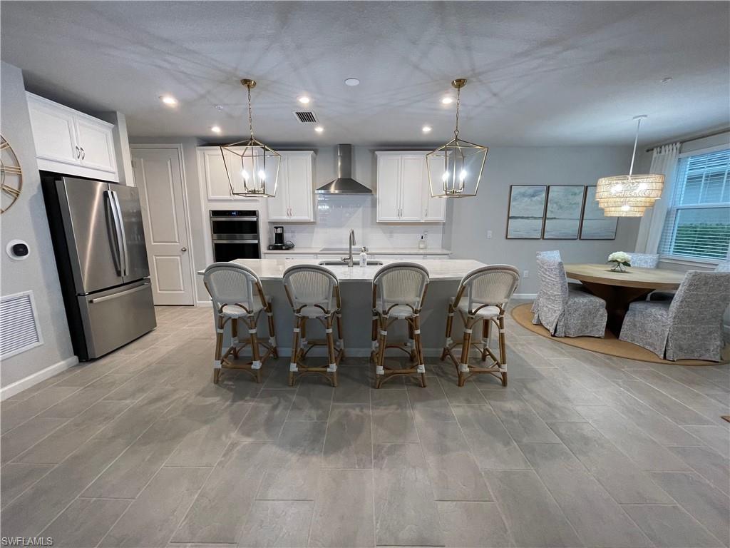 Kitchen with pendant lighting, stainless steel appliances, white cabinetry, recessed lighting, and wall chimney exhaust hood