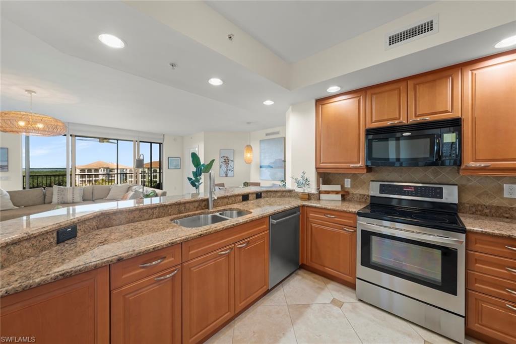 Kitchen featuring stainless steel appliances, recessed lighting, brown cabinetry, and light stone counters