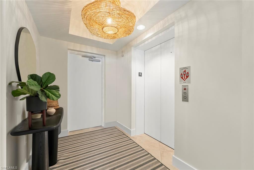 Hallway with light tile patterned flooring, elevator, and a raised ceiling