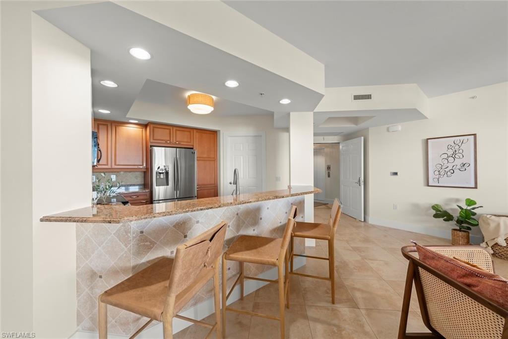 Kitchen featuring a kitchen breakfast bar, light stone counters, stainless steel fridge, brown cabinetry, and a peninsula