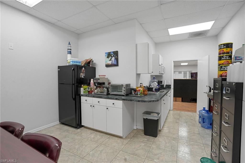 Kitchen with white cabinets, freestanding refrigerator, dark countertops, and a drop ceiling