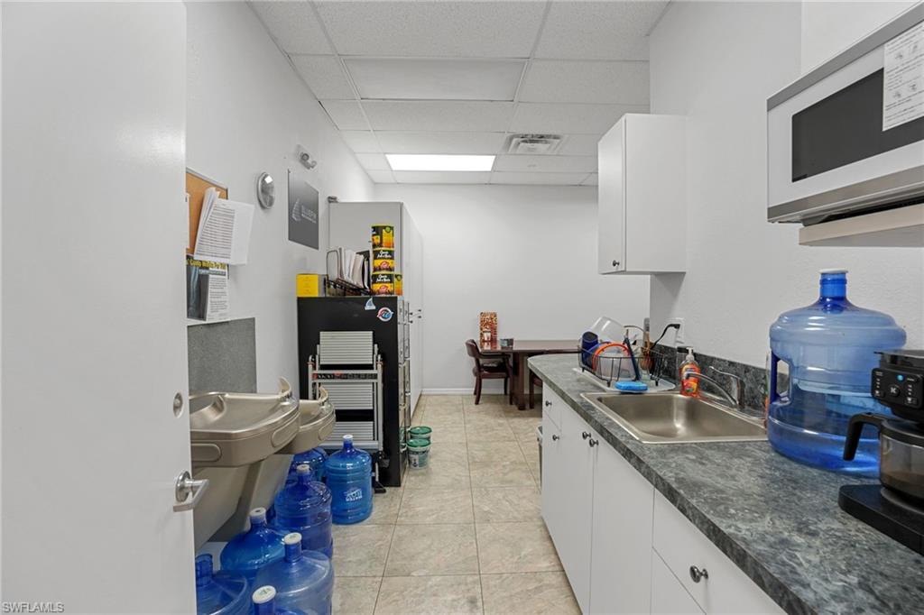 Kitchen with white microwave, a drop ceiling, white cabinetry, light tile patterned flooring, and dark countertops
