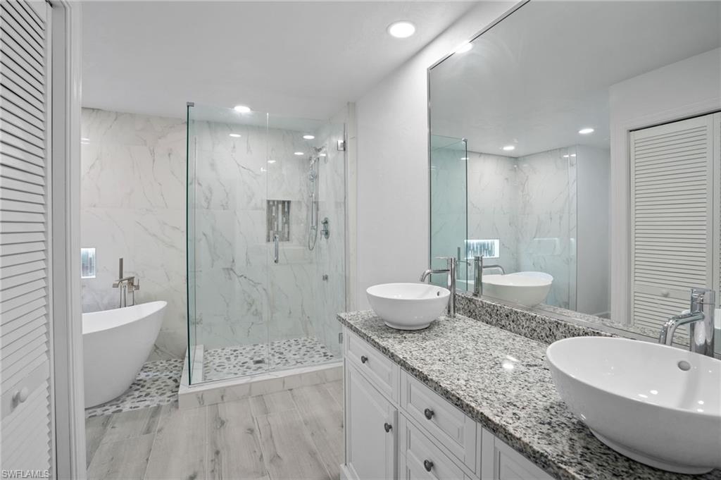 Bathroom featuring a closet, double vanity, a freestanding tub, a marble finish shower, and recessed lighting