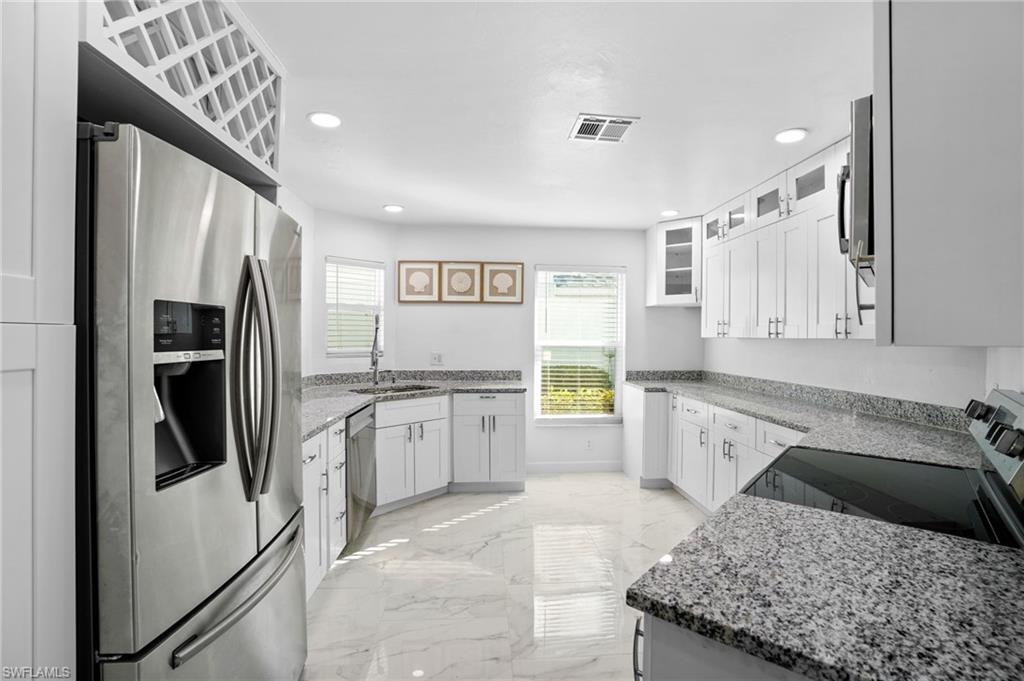 Kitchen with light stone counters, stainless steel appliances, glass insert cabinets, white cabinetry, and recessed lighting