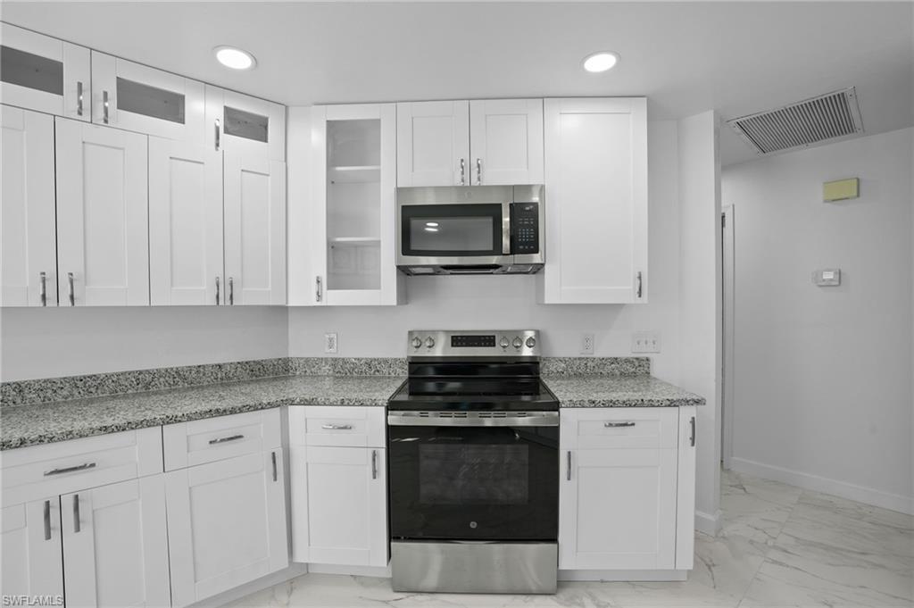 Kitchen featuring appliances with stainless steel finishes, white cabinetry, light stone countertops, glass insert cabinets, and light marble finish floors