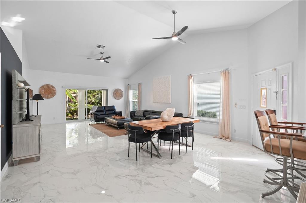 Dining space with high vaulted ceiling, light marble finish flooring, and ceiling fan