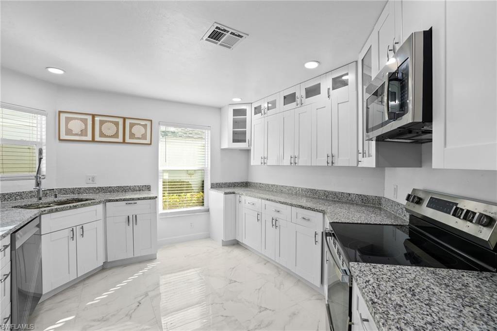 Kitchen featuring appliances with stainless steel finishes, light stone countertops, glass insert cabinets, light marble finish flooring, and recessed lighting