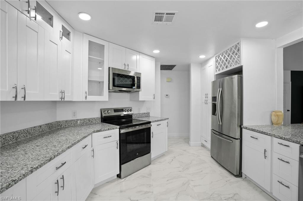 Kitchen with glass insert cabinets, appliances with stainless steel finishes, light stone counters, and recessed lighting