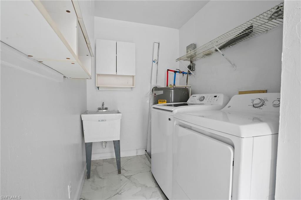Laundry room with light marble finish floors, cabinet space, washing machine and dryer, and electric water heater