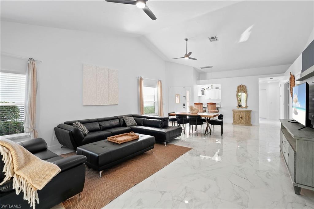 Living room featuring high vaulted ceiling, a ceiling fan, and light marble finish flooring