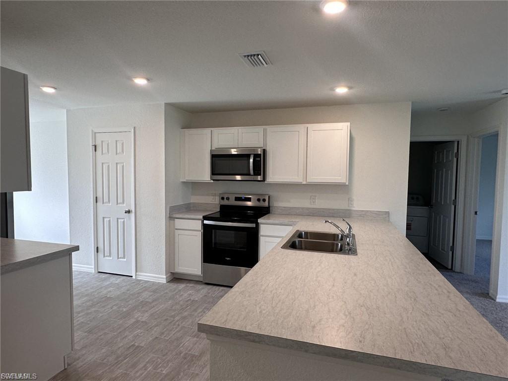 Kitchen featuring appliances with stainless steel finishes, light countertops, white cabinetry, a peninsula, and recessed lighting