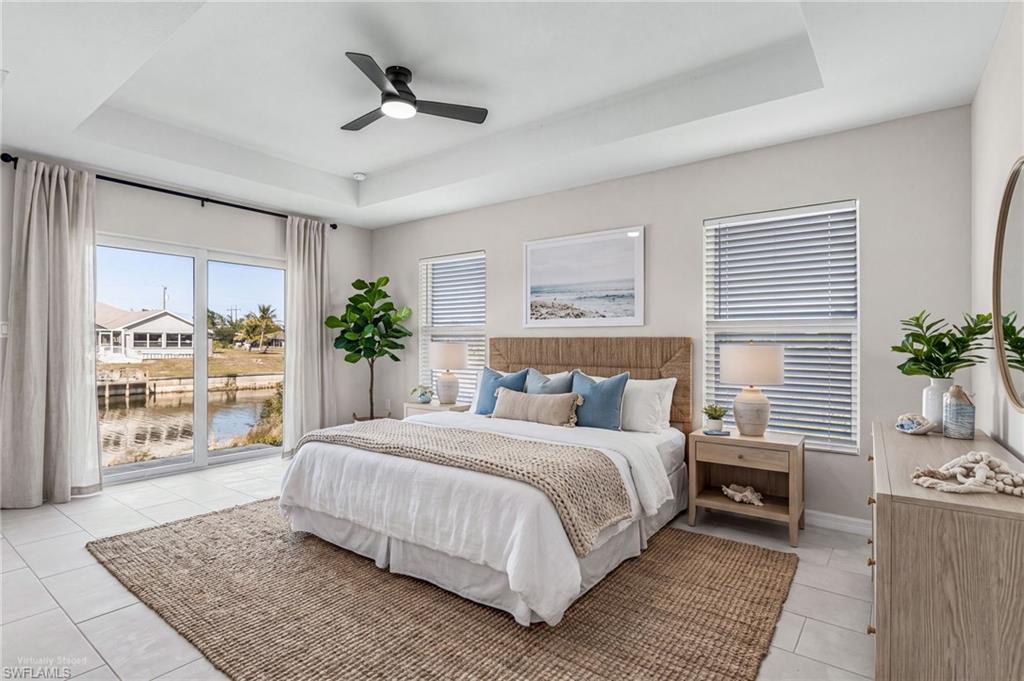 Spacious bedroom featuring a tray ceiling, large sliding glass doors, white tile flooring, and a ceiling fan with integrated lighting