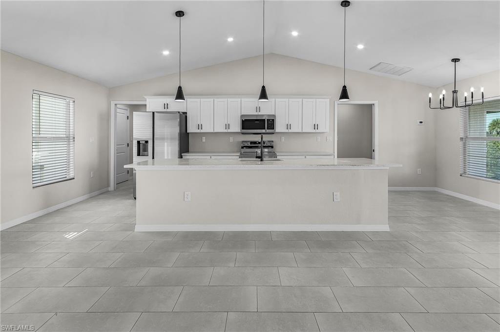 Kitchen featuring white cabinetry, appliances with stainless steel finishes, hanging light fixtures, a large island, and lofted ceiling