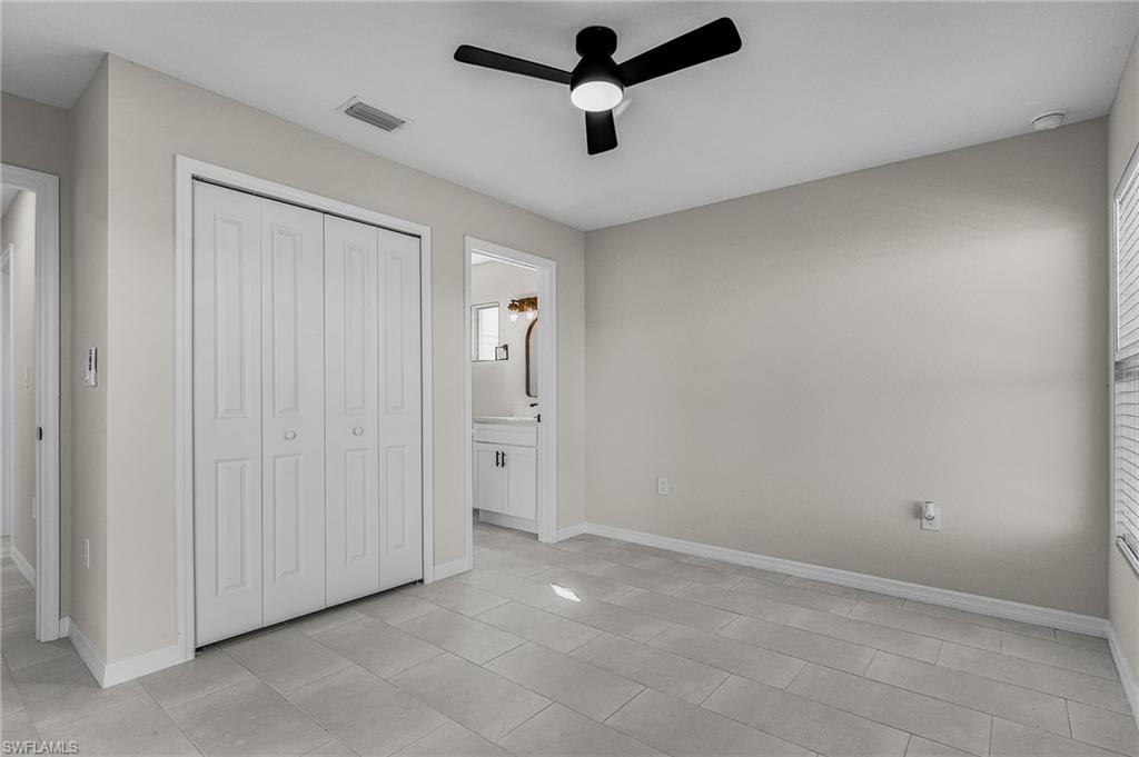 Unfurnished bedroom featuring a closet, a ceiling fan, ensuite bathroom, and light tile patterned floors