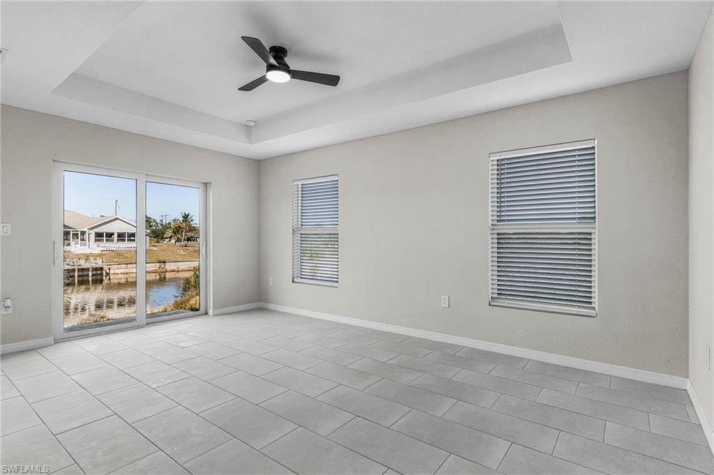 Unfurnished room with a tray ceiling, ceiling fan, a water view, and light tile patterned floors
