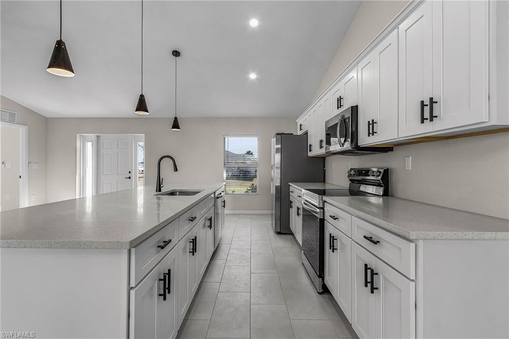 Kitchen with lofted ceiling, appliances with stainless steel finishes, a large island with sink, pendant lighting, and white cabinets