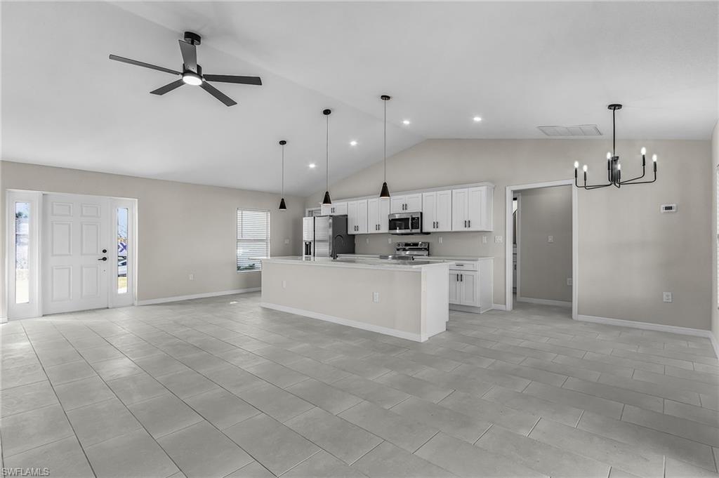 Kitchen with open floor plan, white cabinets, hanging light fixtures, high vaulted ceiling, and a chandelier