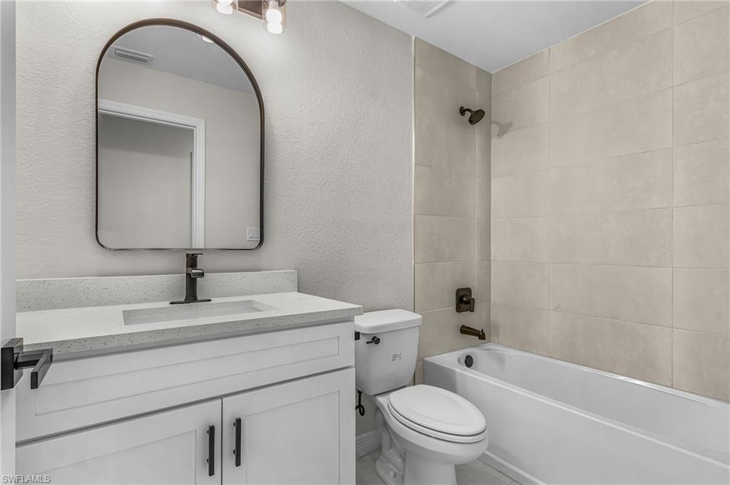 Bathroom featuring a textured wall, vanity, and bathtub / shower combination