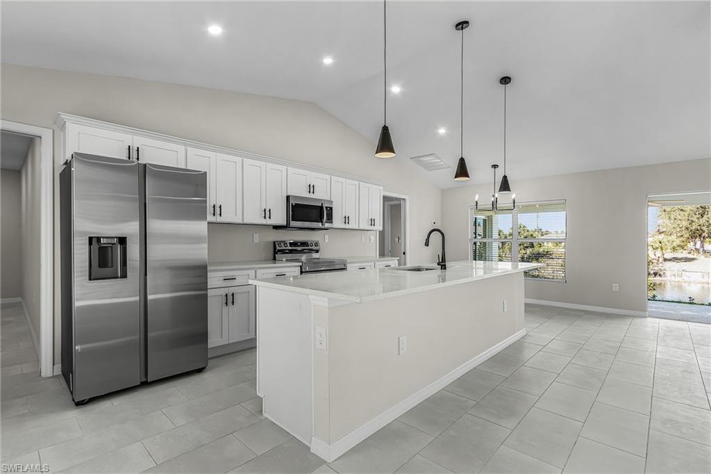 Kitchen with appliances with stainless steel finishes, white cabinets, light stone countertops, a center island with sink, and decorative light fixtures