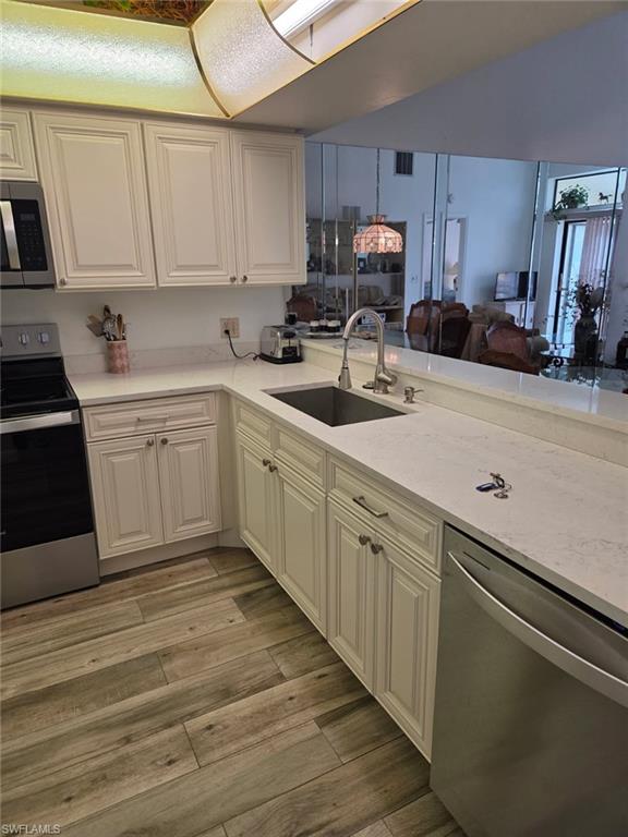 Kitchen featuring stainless steel appliances, light stone counters, open floor plan, light wood-style flooring, and lofted ceiling