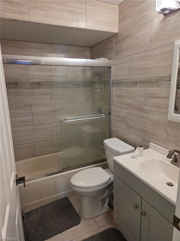 Bathroom with vanity, tile walls, and shower / bath combination with glass door