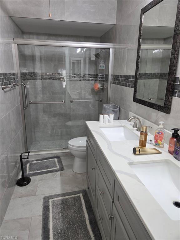 Bathroom with double vanity, a stall shower, and tile walls