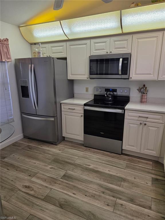 Kitchen featuring appliances with stainless steel finishes, light countertops, light wood finished floors, and white cabinets