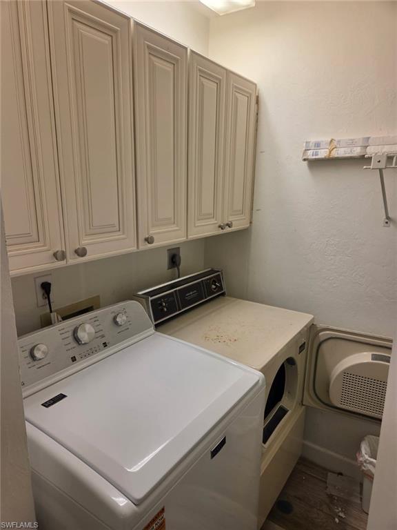 Laundry room with washer and clothes dryer, a textured wall, cabinet space, and dark wood-type flooring