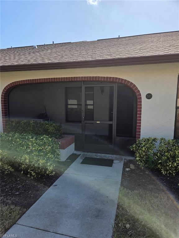 Entrance to property featuring roof with shingles and stucco siding