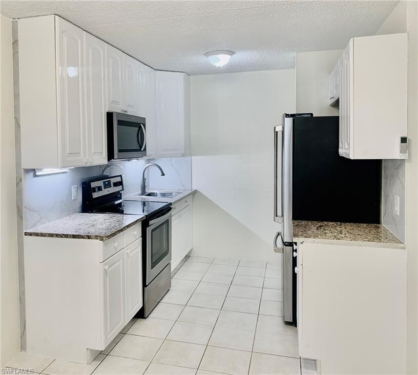 Kitchen featuring appliances with stainless steel finishes, a textured ceiling, light stone counters, tasteful backsplash, and white cabinets