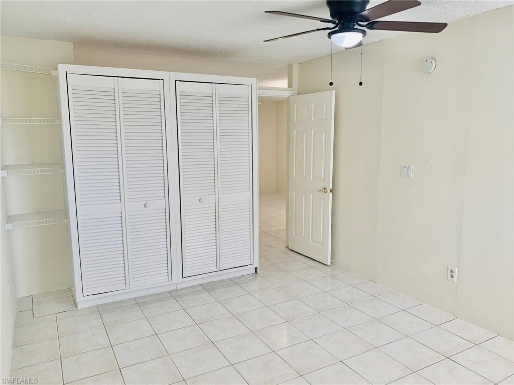 Unfurnished bedroom featuring a ceiling fan, a textured ceiling, light tile patterned floors, and two closets