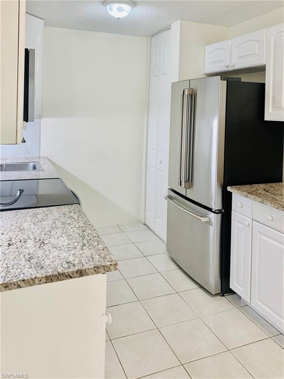 Kitchen featuring freestanding refrigerator, a textured ceiling, light stone counters, white cabinets, and black range with electric stovetop