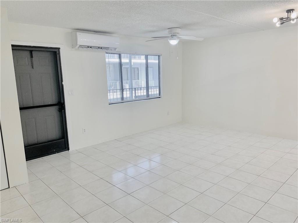 Spare room with a textured ceiling, a wall mounted air conditioner, light tile patterned flooring, and ceiling fan
