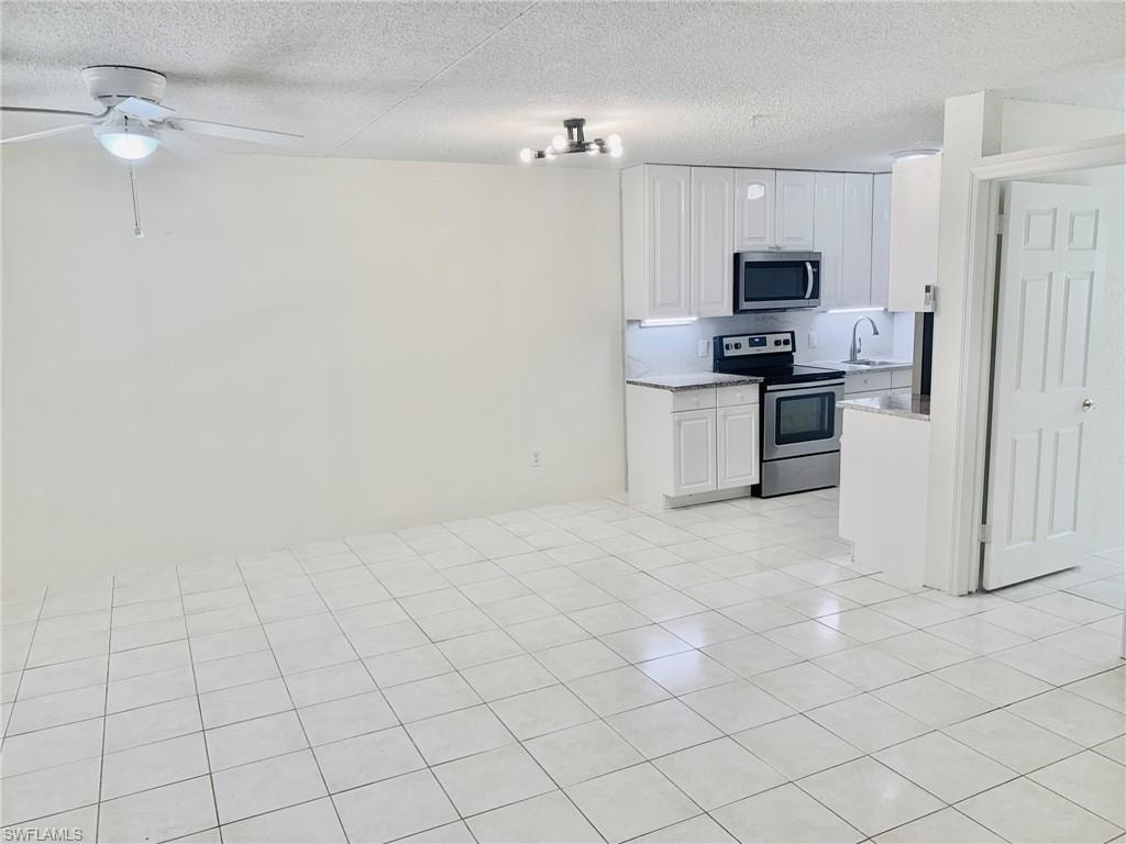 Kitchen featuring stainless steel appliances, white cabinetry, a textured ceiling, light stone countertops, and light tile patterned flooring