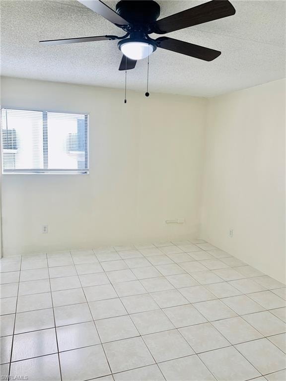 Empty room with a textured ceiling, a ceiling fan, and light tile patterned floors