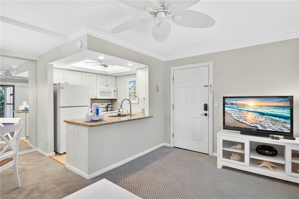 Kitchen featuring white appliances, a peninsula, light carpet, light stone countertops, and crown molding