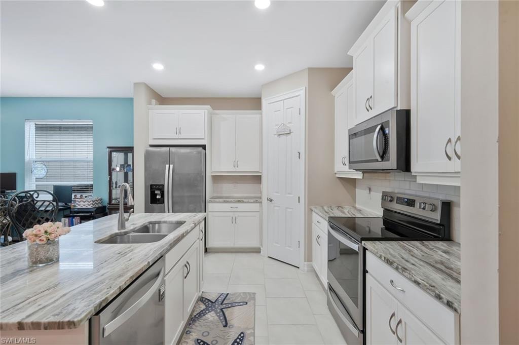 Kitchen featuring appliances with stainless steel finishes, white cabinetry, light stone countertops, a kitchen island with sink, and recessed lighting