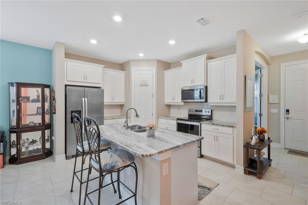 Kitchen featuring stainless steel appliances, white cabinets, light stone counters, a kitchen bar, and recessed lighting