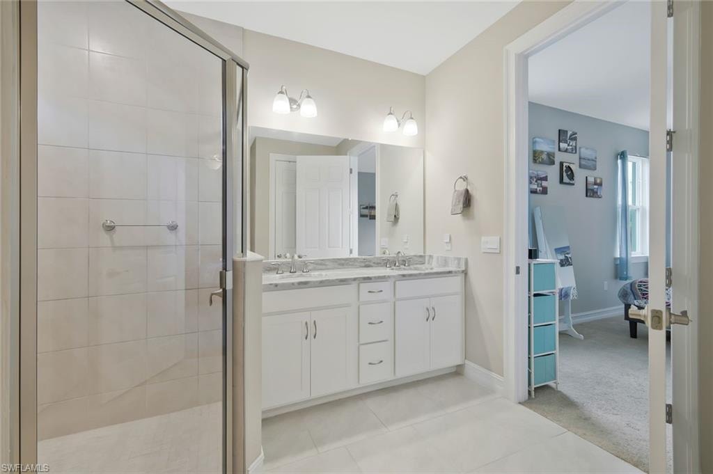 Ensuite bathroom featuring double vanity, a stall shower, light tile patterned flooring, and light carpet