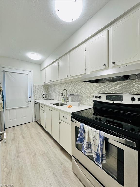Kitchen with stainless steel appliances, white cabinets, light wood-style flooring, under cabinet range hood, and a textured ceiling