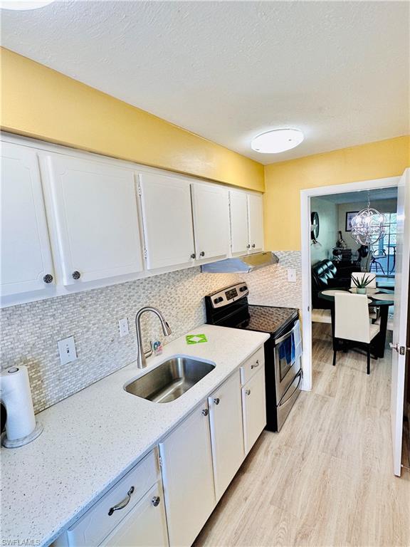 Kitchen with electric range, white cabinets, light wood-style flooring, decorative backsplash, and a chandelier