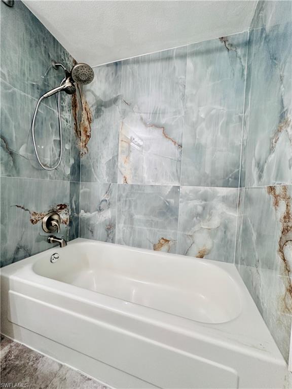 Full bath featuring shower / bathtub combination, a textured ceiling, and tile walls