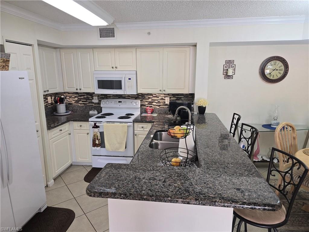 Kitchen with a sink, white appliances, a peninsula, tasteful backsplash, and visible vents
