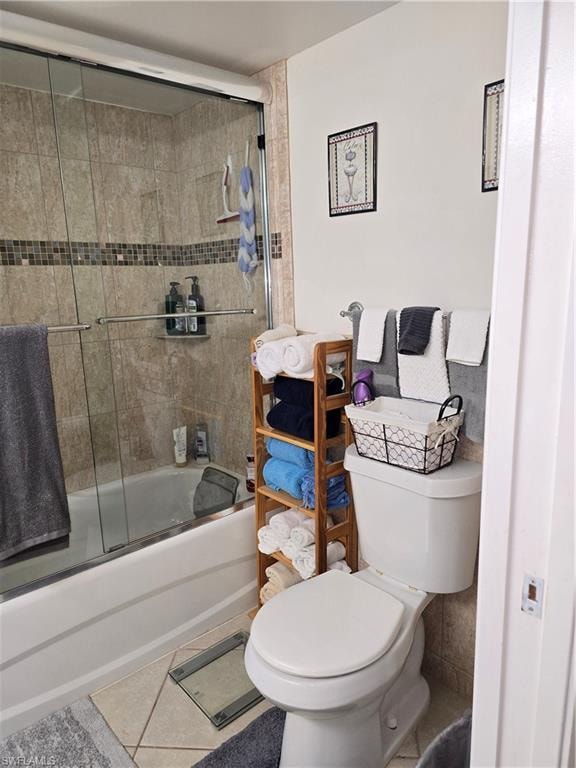 Bathroom featuring combined bath / shower with glass door, tile patterned floors, and toilet